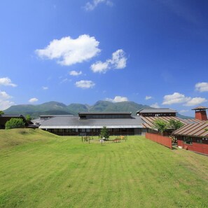 A traditional building with a sloped roof, surrounded by a grassy area and mountains in the background. - Kujukogen Cottage (Taketa)