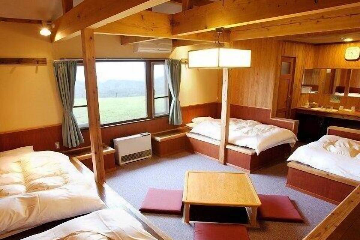 Una cabaña con tres camas, una mesita y un ventanal con cortinas.
