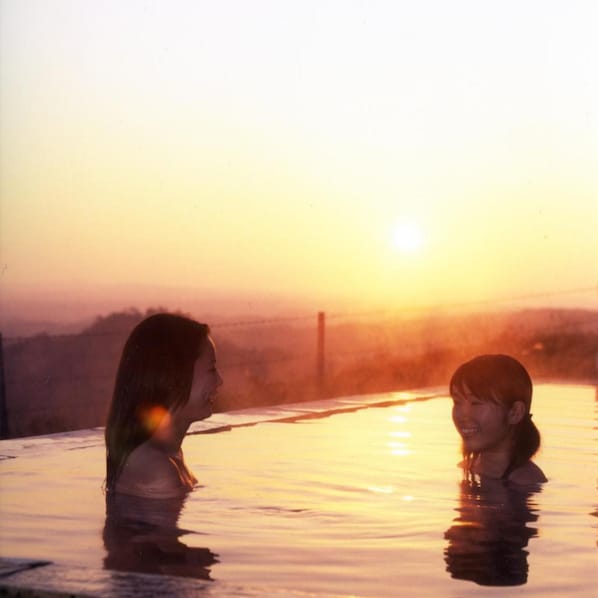 Two individuals in a hot spring with a sunset in the background.
