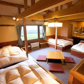 A room with wooden beams, two beds, a small table, and a window with curtains.