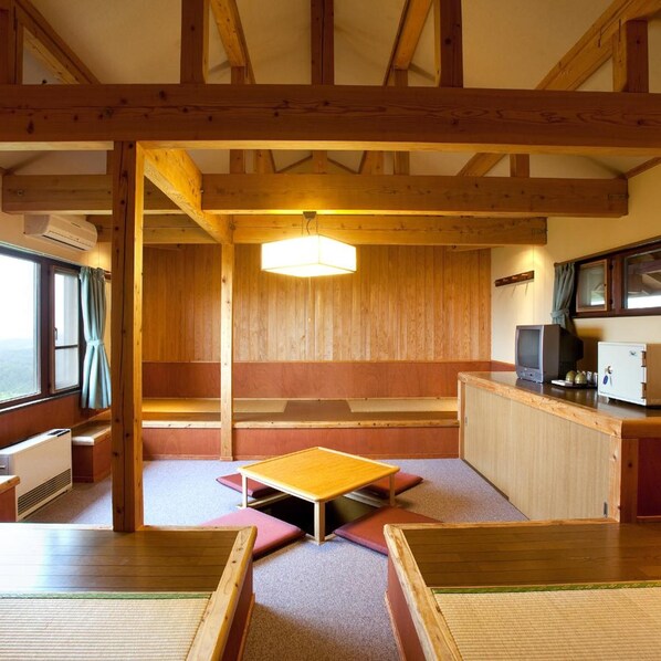 A room with a wooden ceiling, a central table, a television, and a cabinet.
