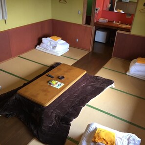A traditional Japanese-style room with tatami flooring, a futon bed, a small wooden table with a remote control, and a pillow with a yellow tag. - Kujukogen Cottage (Taketa)