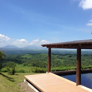 A wooden deck with a pool, overlooking a lush green landscape and distant mountains.