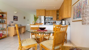 A modern kitchen with wooden cabinets, a glass dining table, and wicker chairs.