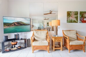 A living room with a television, two wicker chairs, a table with a lamp, and artwork on the wall.