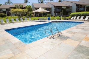 A swimming pool with lounge chairs and umbrellas, surrounded by a fence and greenery.