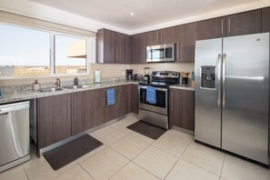 A modern kitchen with dark wood cabinets, stainless steel appliances, and a large window providing a view of the desert landscape. - Relaxing, Quiet Ocean View Condo in Las Conchas with all the amenities (Puerto Peñasco)