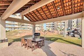 Una terrazza esterna con tavolo e sedie di legno, un barbecue e vista su una collina e edifici sullo sfondo.