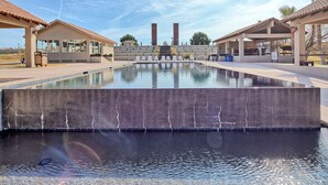 A swimming pool with a stone facade, a covered seating area, and a view of the surrounding landscape.