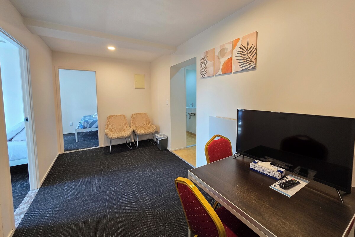 Habitación de hotel con cama, dos sillas, televisor y escritorio con control remoto.