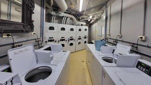 Un cuarto de lavandería con varias lavadoras y secadoras, un espejo y un sistema de ventilación.