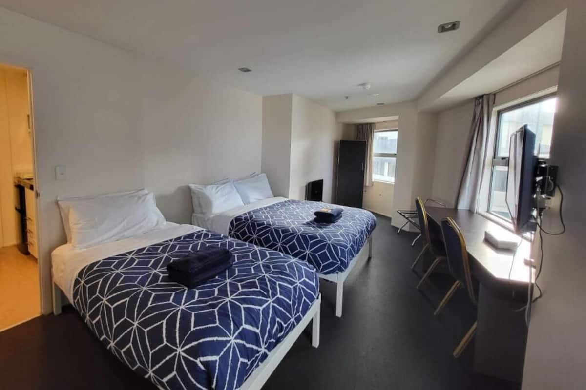 A hotel room with two beds, a desk, and a TV.