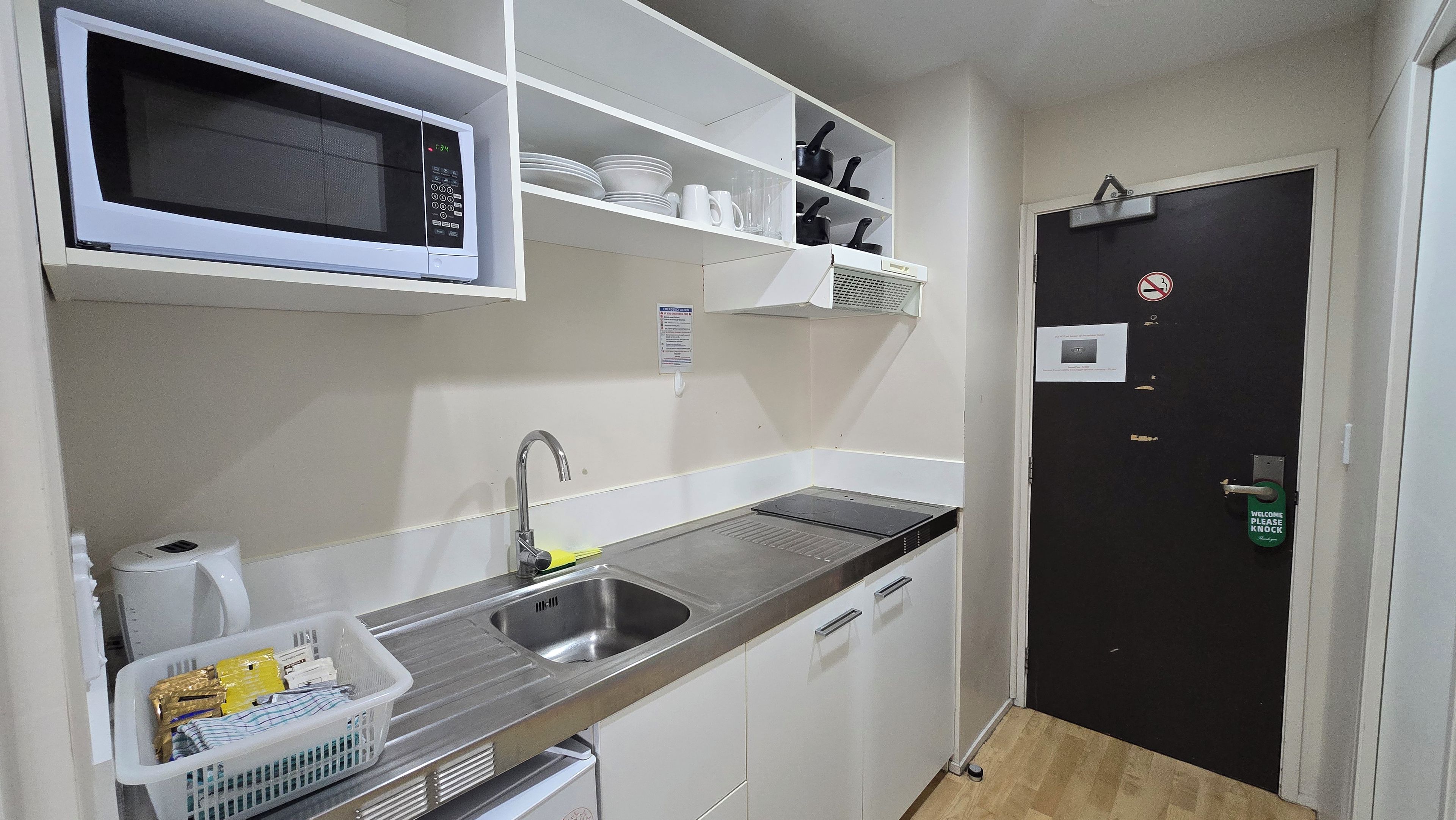 A compact kitchen with a microwave, sink, and storage shelves.