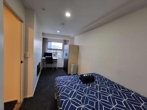 A hotel room with a bed, a desk, and a view of the city. - Empire Apartments (Auckland)
