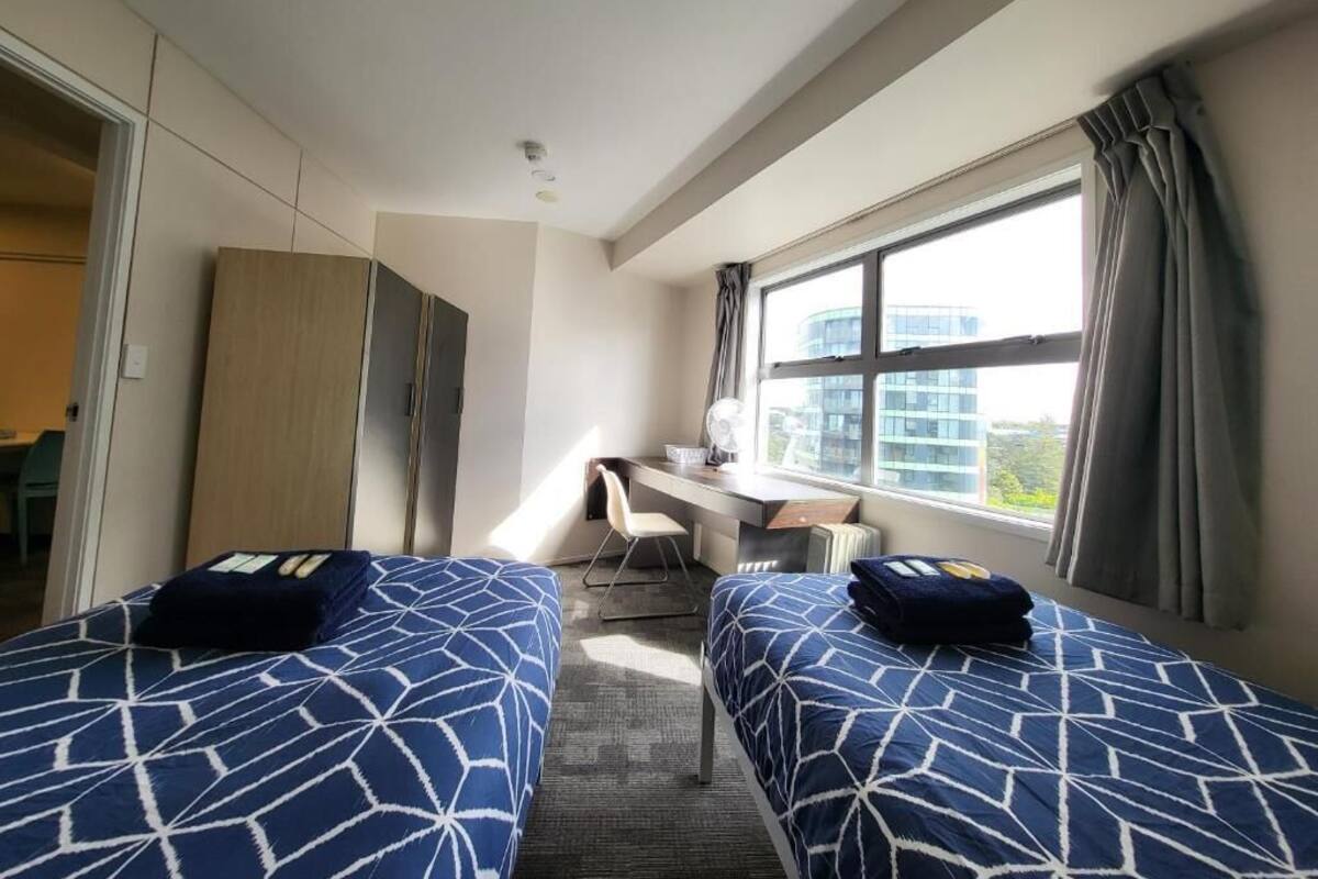 A hotel room with two beds, a desk, a chair, and a large window.
