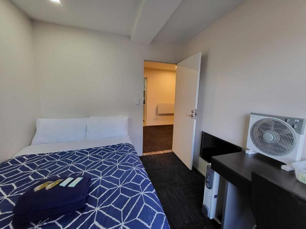 A hotel room with a bed, a desk, a fan, and a bathroom visible through an open door.