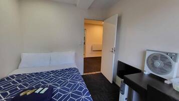 A hotel room with a bed, a desk, a fan, and a bathroom visible through an open door.