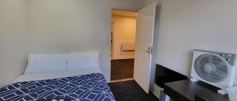 A hotel room with a bed, a desk, a fan, and a bathroom visible through an open door.
