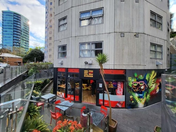 Un restaurant de burgers avec une terrasse, situé à proximité d’un bâtiment moderne doté d’une façade en verre.