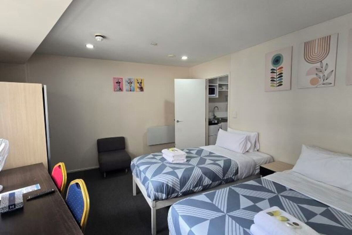 A hotel room with two beds, a desk, a chair, and a wardrobe.