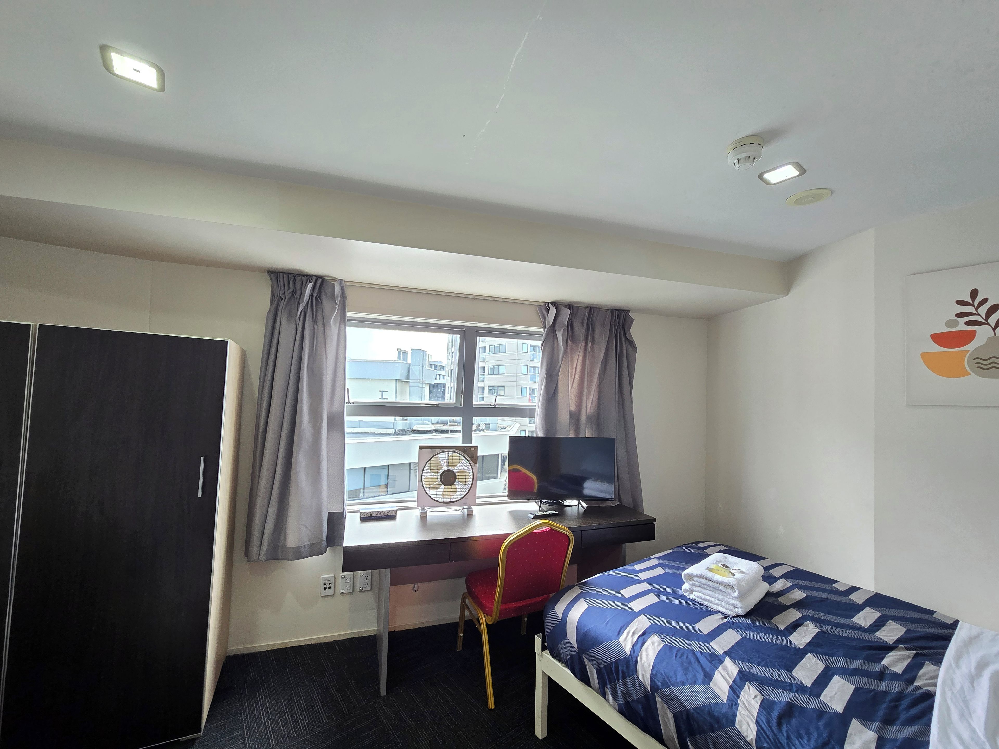 A hotel room with a bed, a desk, a chair, a TV, and a window with curtains.