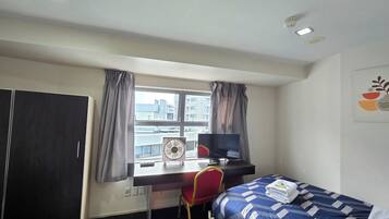 A hotel room with a bed, a desk, a chair, a TV, and a window with curtains.