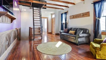 Amplia sala de estar con piso de madera, un sofá de cuero, un sillón amarillo y una escalera que conduce a un nivel superior.