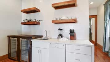 Una cocina con armarios blancos, estantes de madera, lavavajillas y refrigerador.