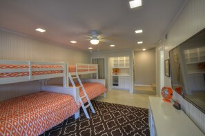 A room with bunk beds, a desk, a mirror, and a ceiling fan.
