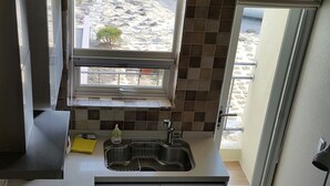 A compact kitchen with a window, a sink, and a refrigerator. - Beanfield House (Seogwipo)