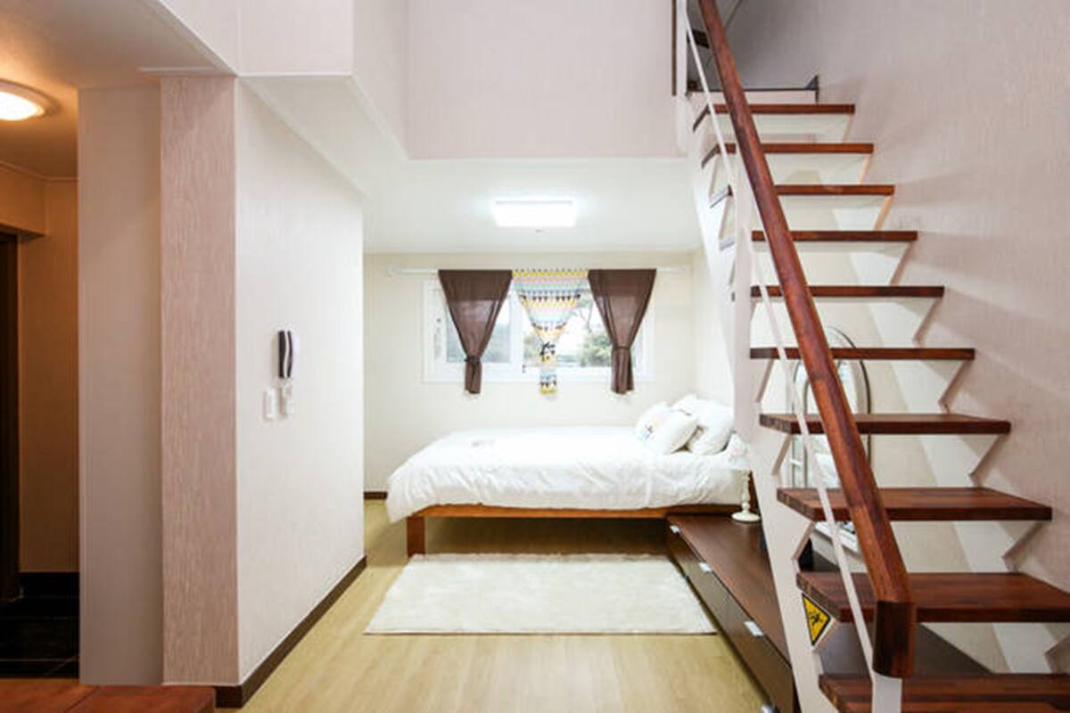 A bedroom with a wooden bed, a white rug, a staircase, and a window with curtains.