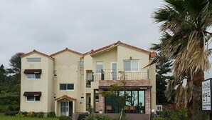 A two-story building with a flat roof, a balcony on the upper floor, and a small front garden. - Beanfield House (Seogwipo)