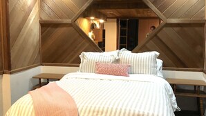 Een slaapkamer met een bed, een bankje en een houten plafondconstructie.