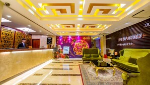 A hotel lobby with a reception desk, green sofas, a patterned rug, and a Christmas-themed wall decoration. - Louis Hotel Zhongshan (Zhongshan)