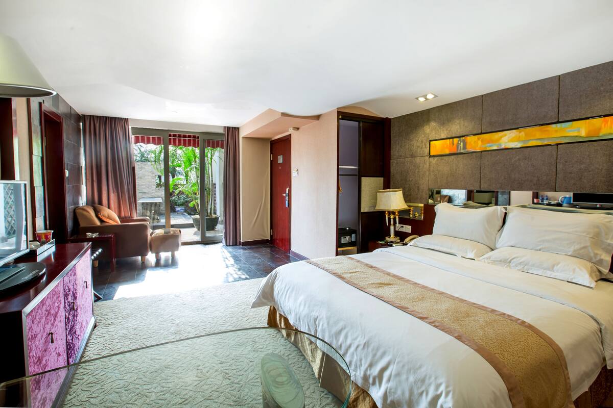 Habitación de hotel con una cama grande, un escritorio con ordenador, una silla, televisión y vistas al exterior.