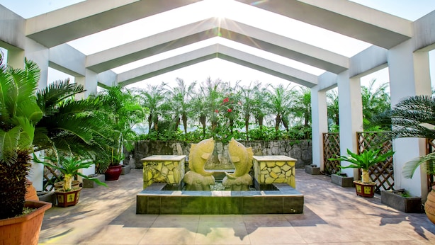 A covered outdoor area with a central water feature and stone sculptures, surrounded by potted plants and a stone wall. - Louis Hotel Zhongshan (Zhongshan)