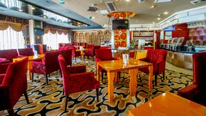A restaurant with red upholstered chairs and tables, a patterned carpet, and a bar area with a red and gold design. - Louis Hotel Zhongshan (Zhongshan)