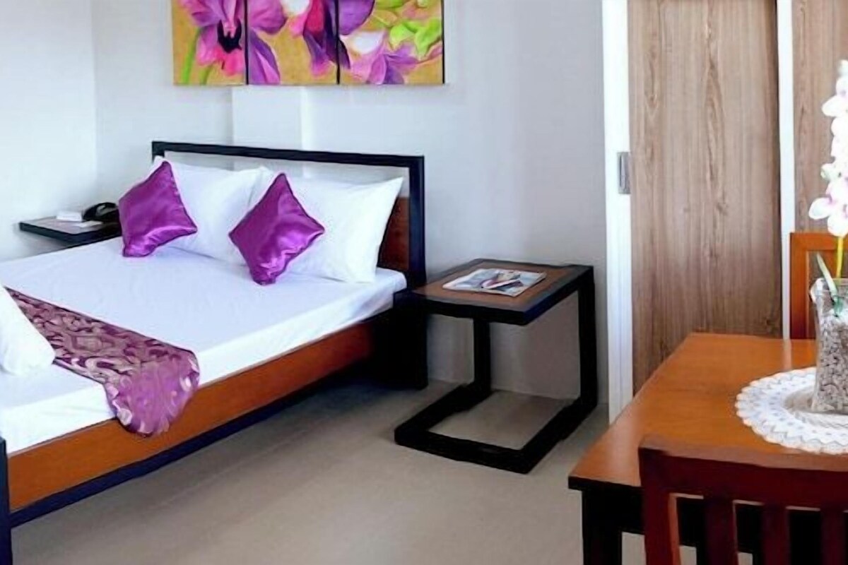 Habitación de hotel con cama, mesitas de noche, un escritorio pequeño, una silla, televisor, zona de cocina y baño.