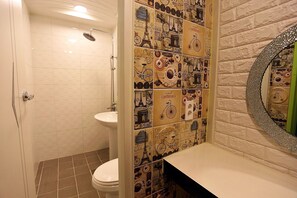 Un baño con ducha, inodoro y lavamanos con espejo. Las paredes están decoradas con diversos diseños e imágenes.