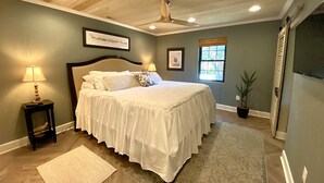 Une chambre avec un grand lit, un ventilateur de plafond, une fenêtre et une table de chevet avec une lampe.