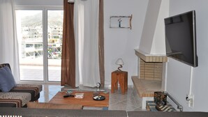 Een woonkamer met een bank, een salontafel, een televisie, een open haard en een uitzicht op gebouwen door een groot raam.
