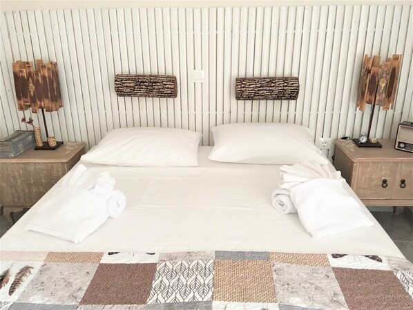 Un lit double avec du linge de lit blanc, deux tables de chevet avec des lampes et une courtepointe à motifs patchwork.