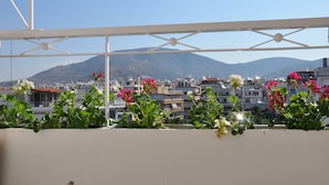 Een balkon met potplanten en bloemen, met uitzicht op een stadsgezicht met gebouwen en een berg op de achtergrond.