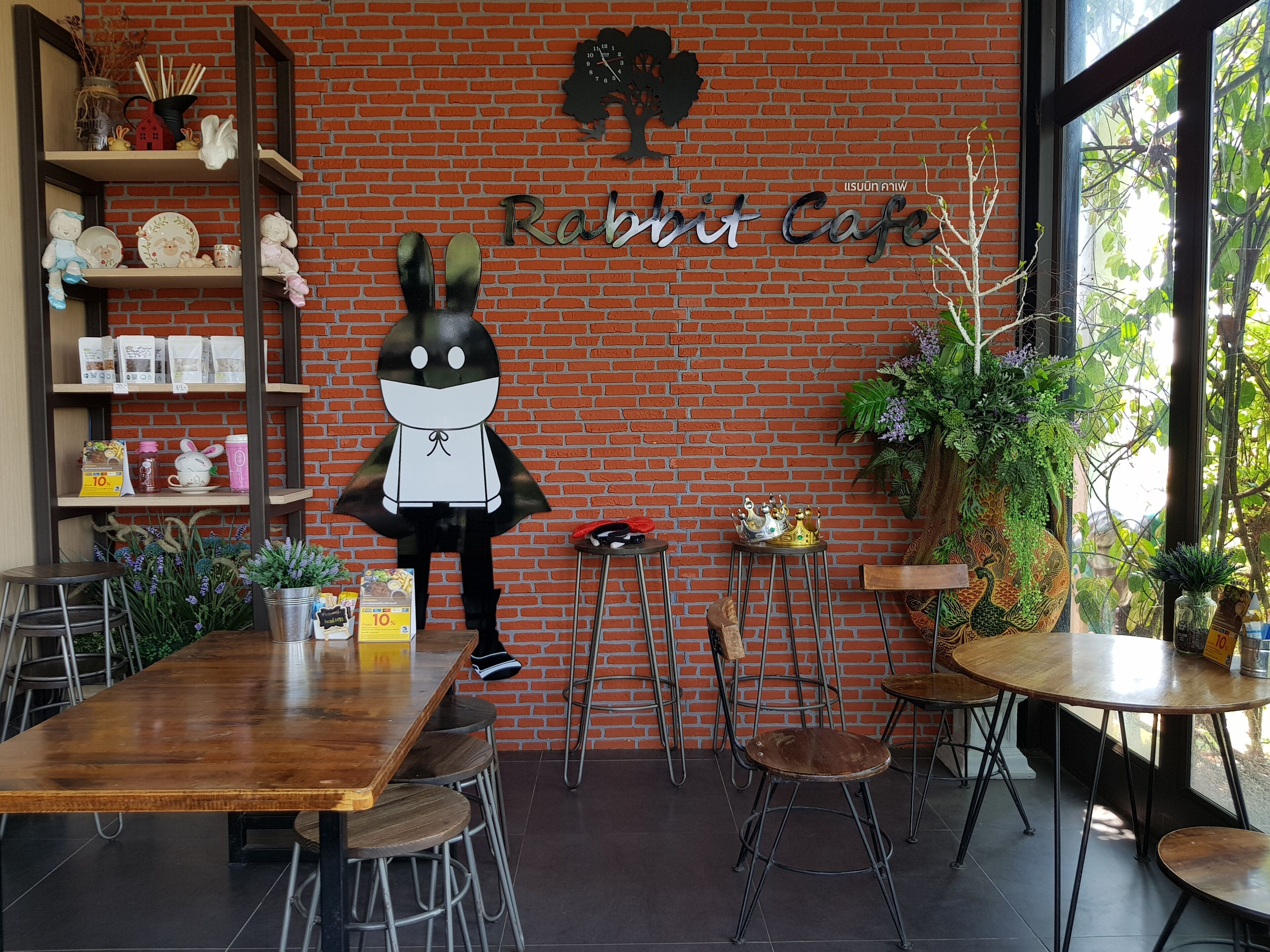Interno di un caffè con parete in mattoni, una mascotte a forma di coniglio e diverse piante.