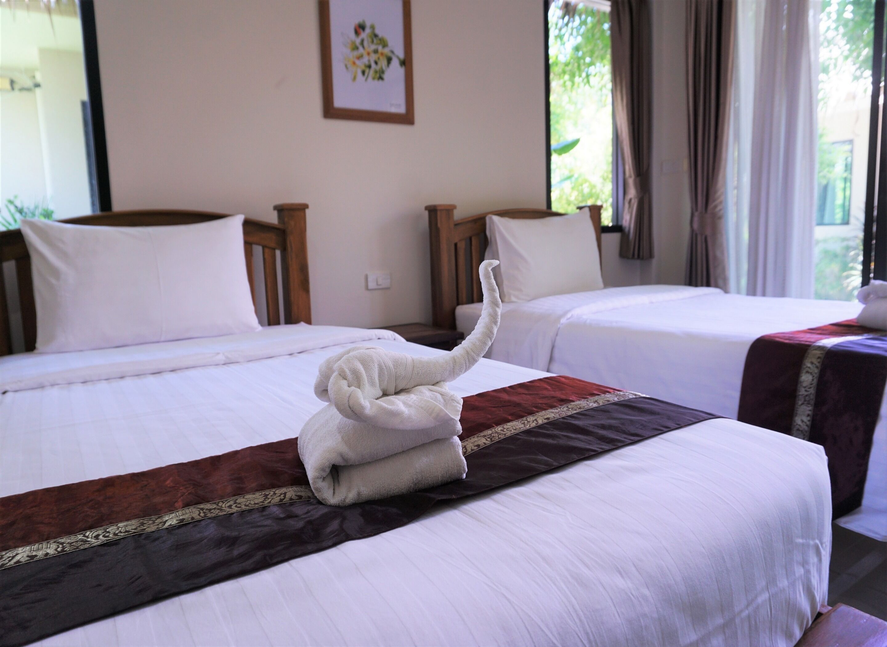 A hotel room with two beds, each with white linens and a brown decorative strip. A towel is placed on the bed in the foreground.