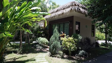 Una casa con techo de paja, rodeada de abundante vegetación y un sendero de piedra que conduce a la entrada.