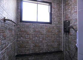 A bathroom with a stone wall, a window, and a shower with a hose.