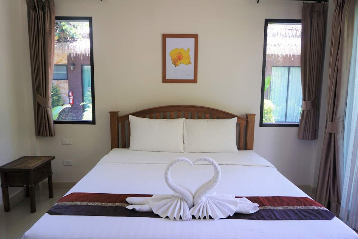 A neatly made bed with a heart-shaped towel arrangement, a wooden headboard, and a framed picture on the wall.