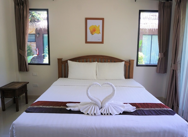 Una cama bien hecha con una decoración de toallas en forma de corazón, un cabecero de madera y un cuadro en la pared.