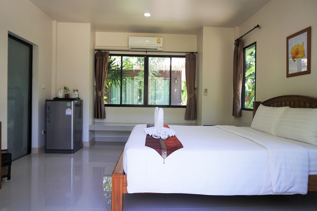 A hotel room with a bed, a refrigerator, a window with curtains, and a wall-mounted air conditioner.